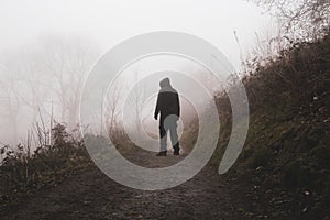 A scary hooded figure. Back to camera. Standing on a path in the countryside. On a spooky foggy winters day