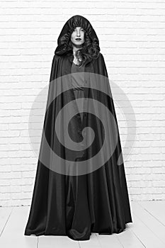 Scary but iconic. A woman witch. Sexy woman wearing halloween costume on white brickwall. Sensual woman with classic