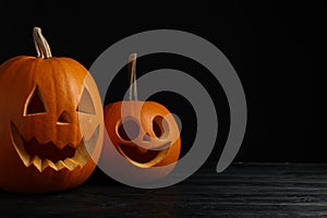 Scary jack o\'lanterns made of pumpkins on wooden table against black background, space for text. Halloween traditional decor
