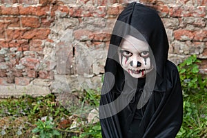 Scary little girl in a little zombie costume looks frighteningly at the camera against a brick wall. copy space. zombie Apo