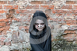 Scary little girl in a little zombie costume looks frighteningly at the camera against a brick wall. copy space. zombie Apo. photo