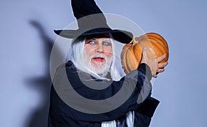 Scary man in witch hat with pumpkin. Demon with Jack o lantern. Happy Halloween. Handsome man in holiday costume.