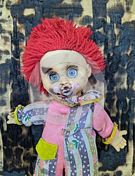 scary and old battered clown doll with burnt face and red hair on the background of burnt wooden board