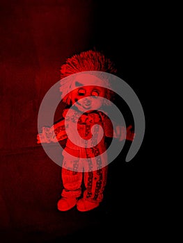 scary and old battered clown doll with burnt face under red and black lighting