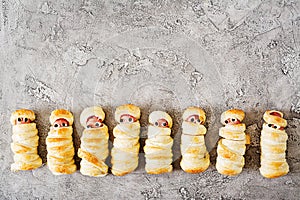 Scary sausage mummies in dough with funny eyes on table.