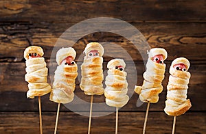 Scary sausage mummies in dough with funny eyes on table.