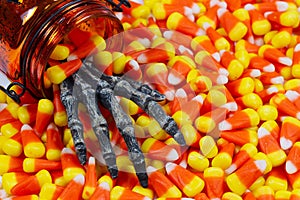 Scary skeleton hand coming out jar into a pile of candy corn