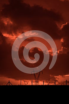 Scary sunset, with red sky and clouds, after storm. Power pylons and industrial fences in devastated landscape. B Evil environment