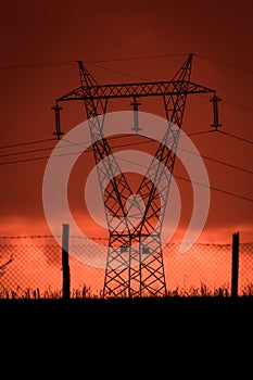 Scary sunset, with red sky and clouds, after storm. Power pylons and industrial fences in devastated landscape. B Evil environment