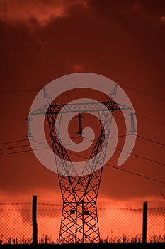 Scary sunset, with red sky and clouds, after storm. Power pylons and industrial fences in devastated landscape. B Evil environment