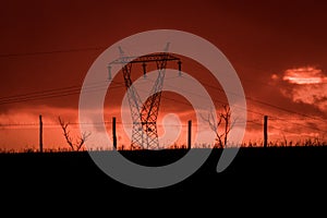 Scary sunset, with red sky and clouds, after storm. Power pylons and industrial fences in devastated landscape. B Evil environment