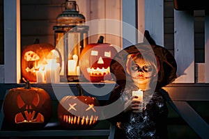 Scary toddler child in halloween costume, playing with carved pumpkins