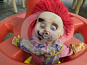 scary toy clown with red hair and half open blue eyes and outstretched hands in a plastic wheel