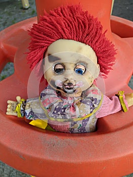 scary toy clown with red hair and half open blue eyes and outstretched hands in a plastic wheel