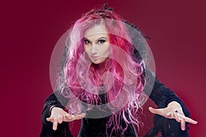 Scary witch with red hair performs magic on a pink background. Halloween, horror theme.