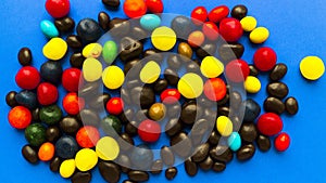Scattered bright multi-colored sweets in the form of jelly beans on a blue background.