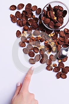 Scattered cacao cereals on ultimate gray background with blank space and hand showing forefinger.