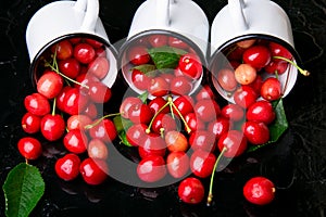 Scattered cherry from enamel cups. Cherries in iron cup on black background. Healthy, summer fruit. Cherries. Three. Close up.