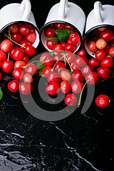 Scattered cherry from enamel cups. Cherries in iron cup on black background. Healthy, summer fruit. Cherries. Three. Close up.