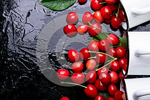 Scattered cherry from enamel cups. Cherries in iron cup on black background. Healthy, summer fruit. Cherries. Three. Top view.