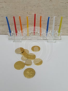 Scattered chocholate coins with a glass hannukiah filled with colourful candles in the background