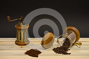 Scattered coffee beans ground coffee and manual coffee grinder on the wooden boards and on black background