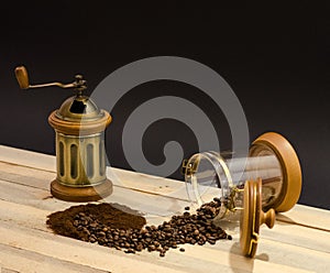 Scattered coffee beans ground coffee and manual coffee grinder on the wooden boards and on black background