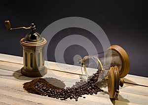 Scattered coffee beans ground coffee and manual coffee grinder on the wooden boards and on black background