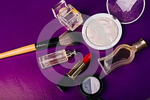 Scattered cosmetics on a purple background. The contents of women`s handbags. Lady set. Lipstick, perfume and shadow. View from