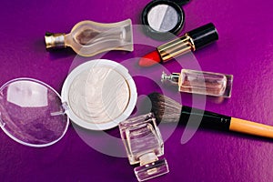 Scattered cosmetics on a purple background. The contents of women`s handbags. Lady set. Lipstick, perfume and shadow. View from