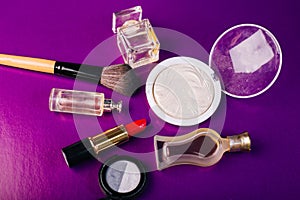 Scattered cosmetics on a purple background. The contents of women`s handbags. Lady set. Lipstick, perfume and shadow. View from