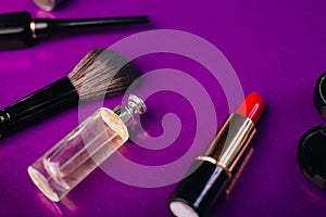 Scattered cosmetics on a purple background. The contents of women`s handbags. Lady set. Lipstick, perfume and shadow. View from