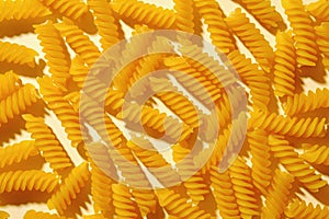 Scattered dried. spiral Italian pasta or noodles on yellow