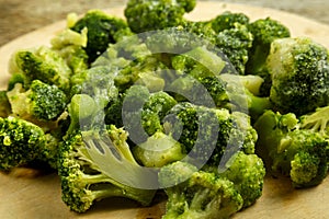 Scattered frozen broccoli on a round wooden board.