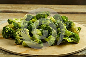 Scattered frozen broccoli on a round wooden board.