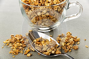 Scattered granola, spoon, muesli in cup on gray table