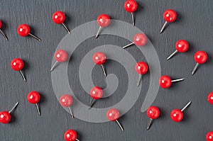 Scattered many red push pins on dark concrete desk in office, school or home