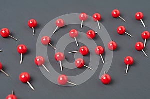 Scattered many red push pins on dark concrete desk in office, school or home