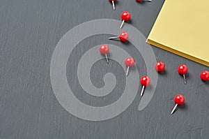 Scattered many red push pins near square blank paper lies on dark concrete desk in office, school or home