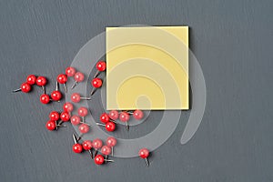 Scattered many red push pins near square blank paper lies on dark concrete desk in office, school or home