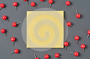 Scattered many red push pins near square blank paper lies on dark concrete desk in office, school or home