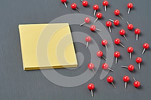 Scattered many red push pins near square blank paper lies on dark concrete desk in office, school or home