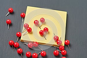 Scattered many red push pins near square blank paper lies on dark concrete desk in office, school or home