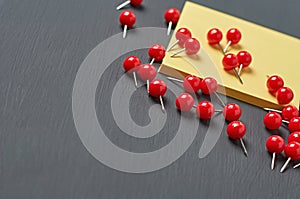 Scattered many red push pins near square blank paper lies on dark concrete desk in office, school or home