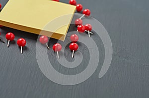 Scattered many red push pins near square blank paper lies on dark concrete desk in office, school or home