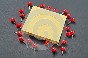 Scattered many red push pins near square blank paper lies on dark concrete desk in office, school or home. Space for text