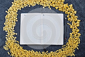 Scattered mixed raw pasta around notebook on blue background