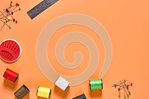 Scattered needles, metal ruler and spools with colorful threads on orange tailors desk in workshop