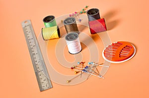 Scattered needles, metal ruler and spools with colorful threads on orange tailors desk in workshop
