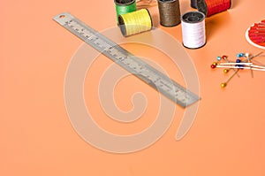 Scattered needles, metal ruler and spools with colorful threads on orange tailors desk in workshop